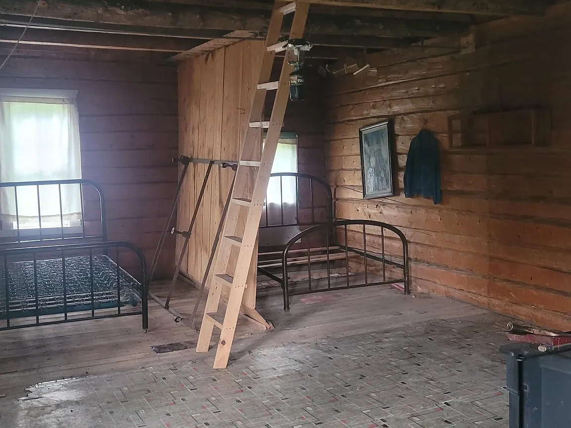 Rustic cabin interior with sleeping areas and a loft ladder